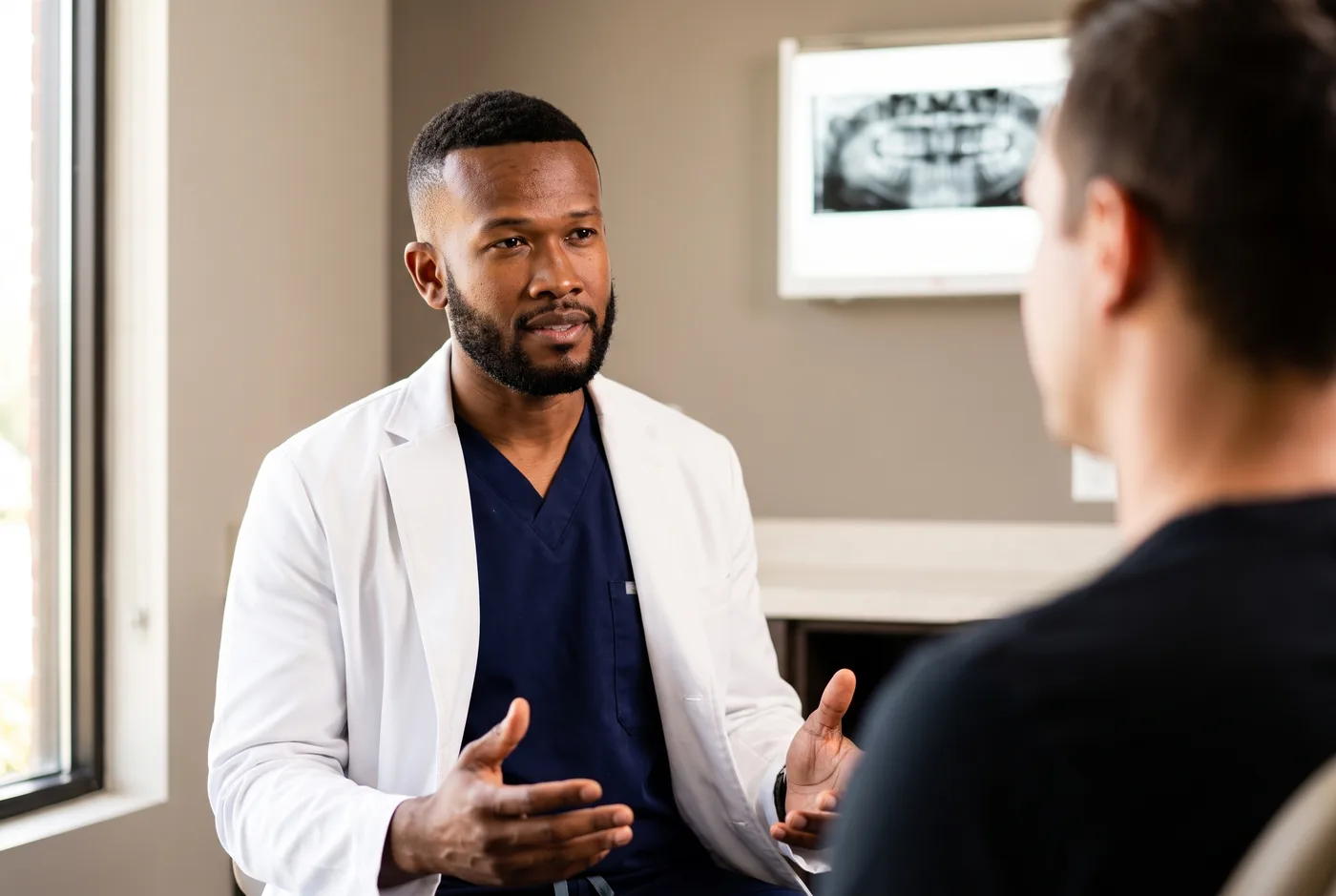 Dr. Peter K. Cudjoe seated in a consultation room, speaking with a patient whose back is to the camera